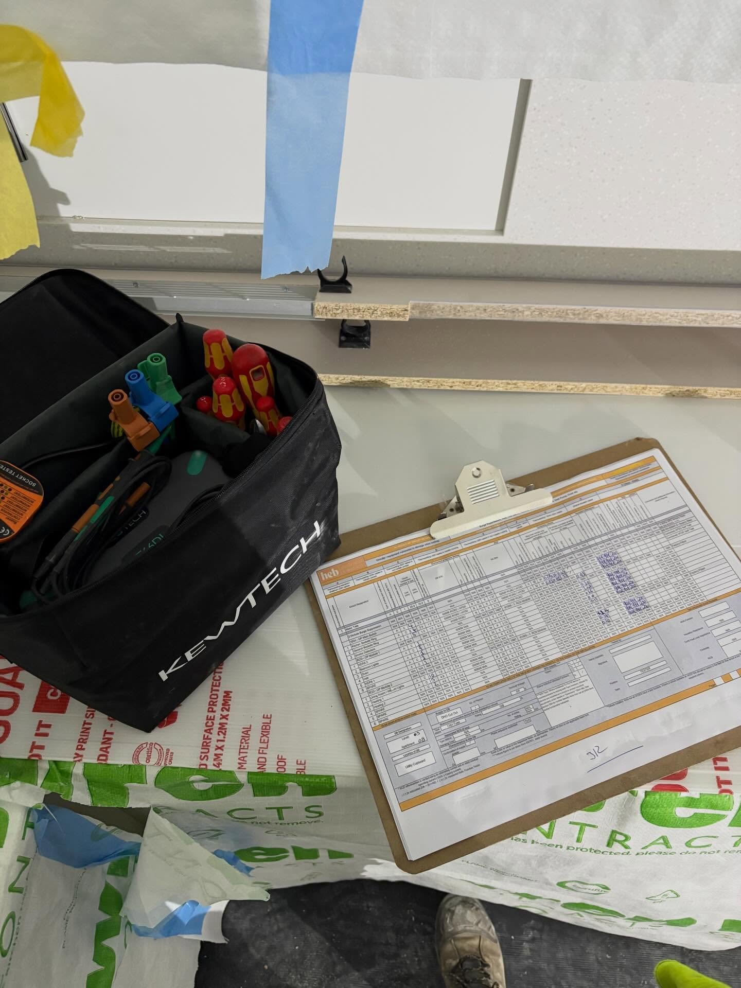 Kewtech tool bag with multifunction tester and EICR documentation on clipboard at job site