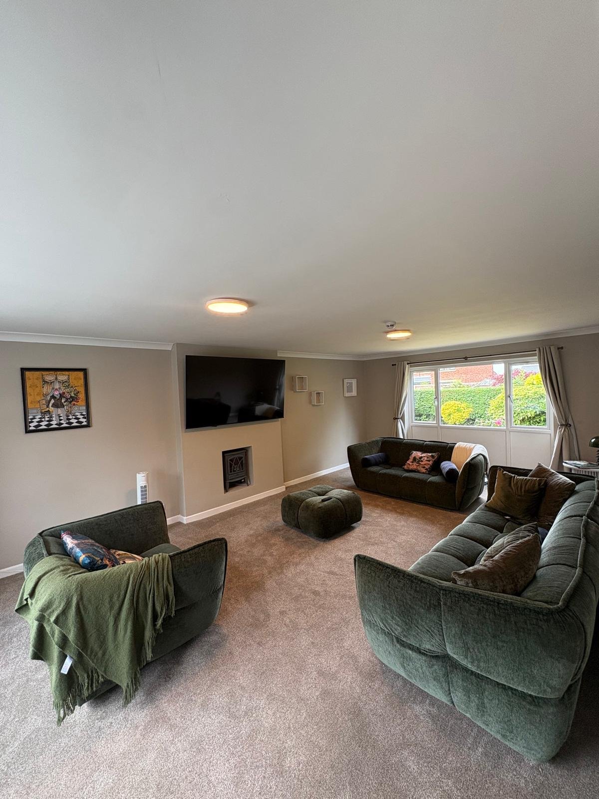 Large living room with two flush LED ceiling lights and wall-mounted TV above fireplace